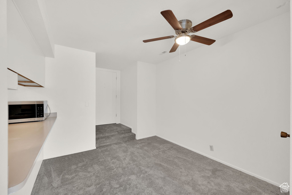 Unfurnished living room featuring ceiling fan and dark carpet