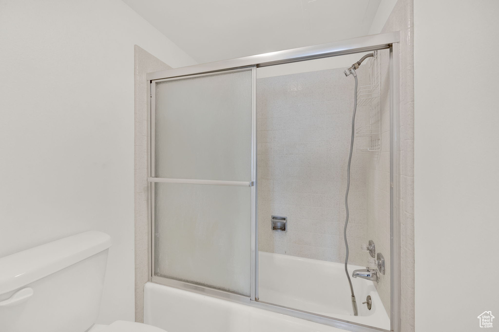 Bathroom featuring toilet and bath / shower combo with glass door