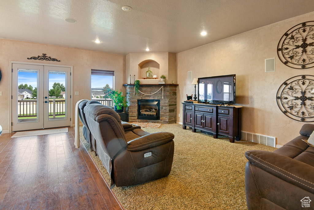 Living room with a stone fireplace, wood-type flooring, a textured ceiling, and french doors