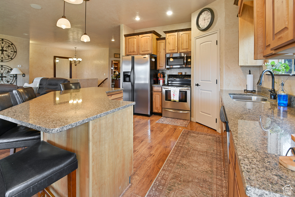 Kitchen with a kitchen bar, appliances with stainless steel finishes, light hardwood / wood-style floors, and sink