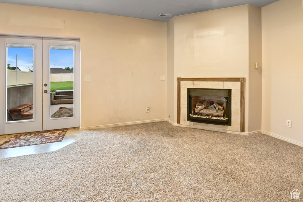 Unfurnished living room with carpet flooring, a tile fireplace, and french doors