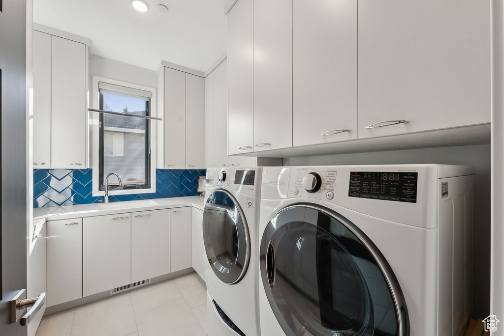 Laundry room featuring washing machine and clothes dryer, cabinet space, and light tile patterned flooring