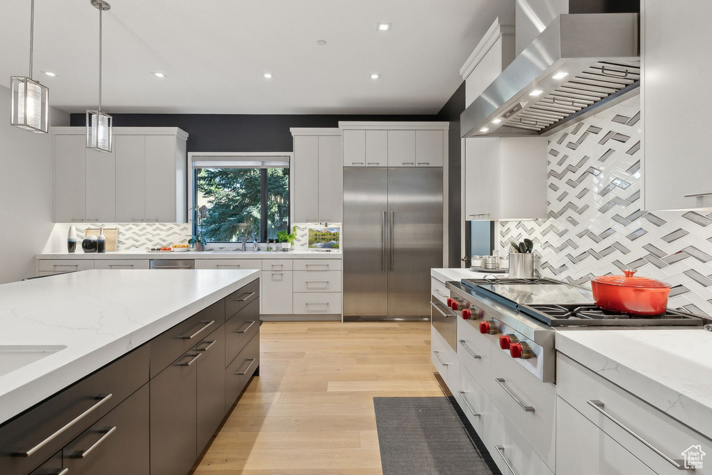 Kitchen with wall chimney exhaust hood, stainless steel appliances, decorative backsplash, white cabinets, and recessed lighting