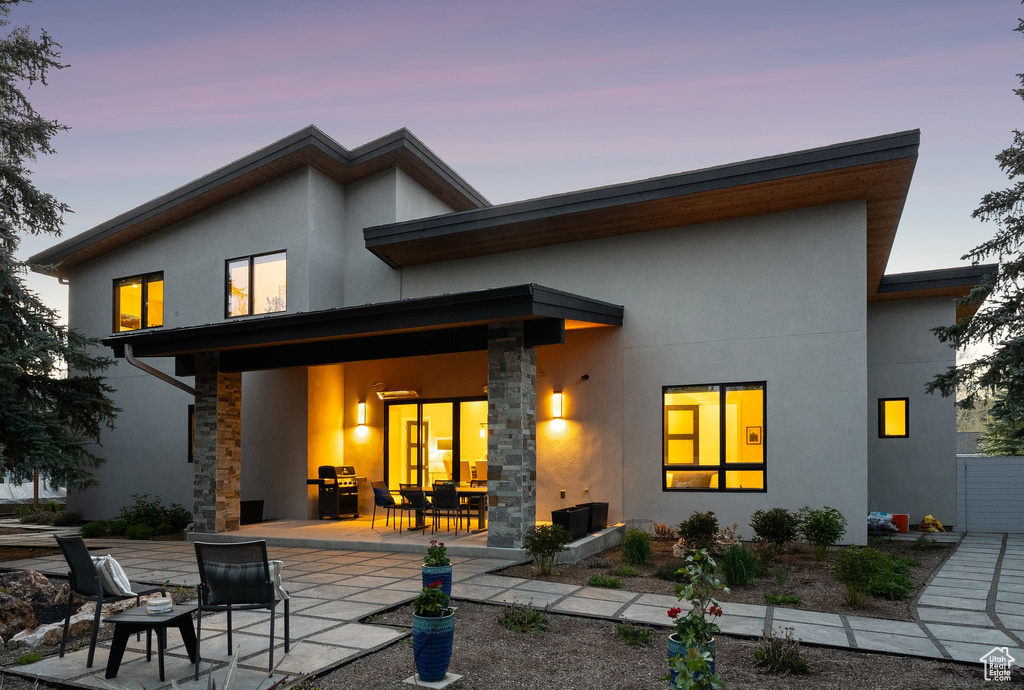 Back of property featuring stucco siding, a patio area, and stone siding