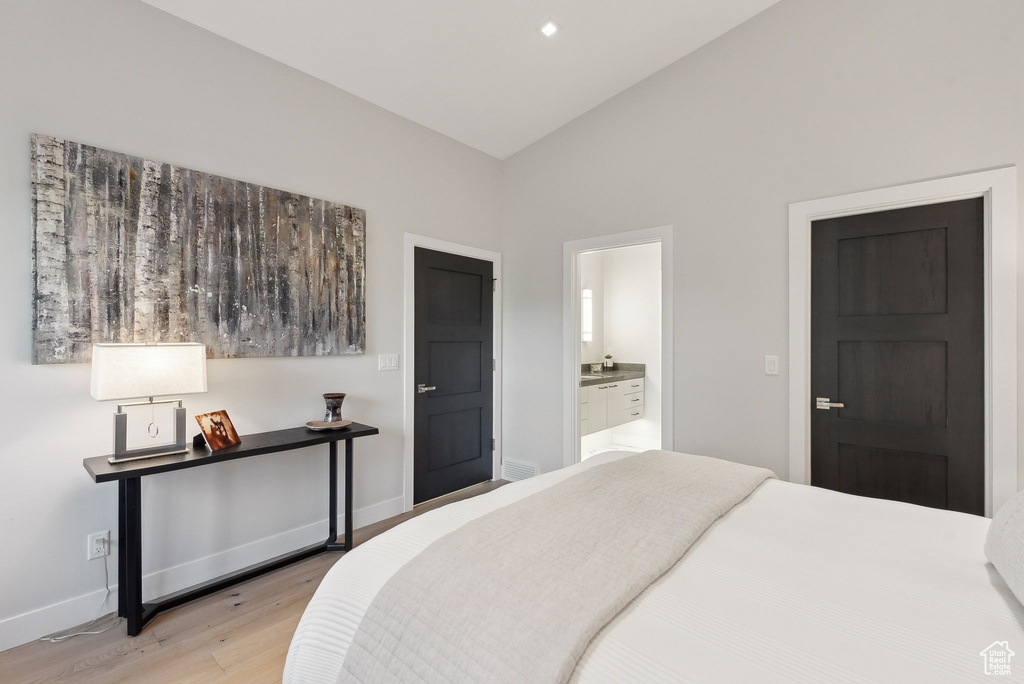 Bedroom featuring light wood-type flooring, baseboards, lofted ceiling, and ensuite bathroom