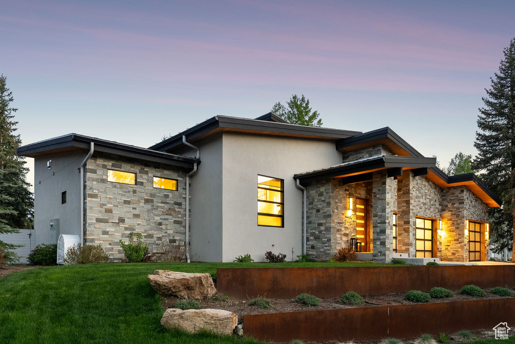 View of front facade with stone siding, stucco siding, and a yard