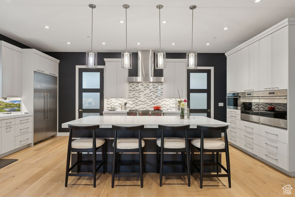 Kitchen featuring wall chimney range hood, appliances with stainless steel finishes, light countertops, decorative backsplash, and recessed lighting