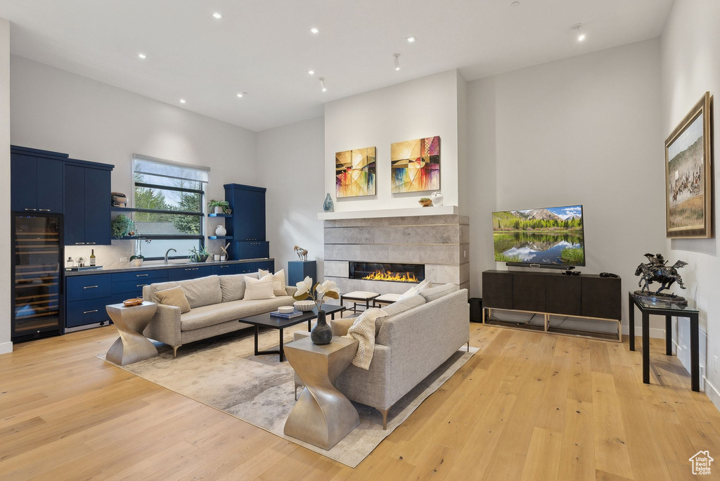 Living area with wine cooler, light wood finished floors, recessed lighting, a fireplace, and a high ceiling