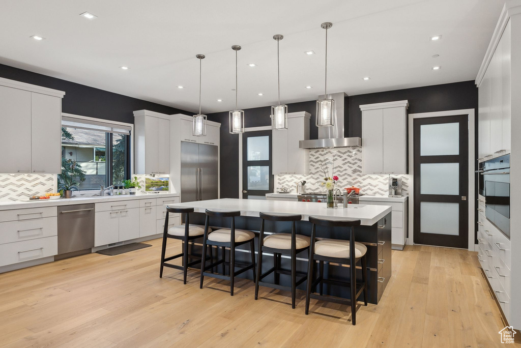 Kitchen featuring wall chimney range hood, stainless steel appliances, tasteful backsplash, light countertops, and recessed lighting