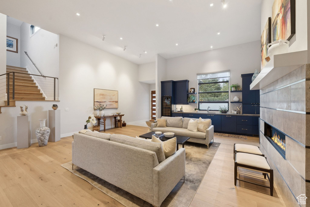 Living room with stairs, light wood-style flooring, a towering ceiling, recessed lighting, and a fireplace