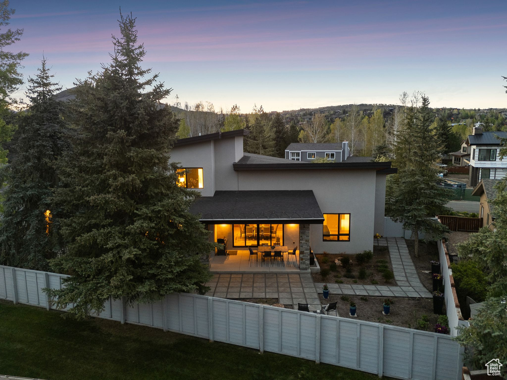 Back of house at dusk featuring stucco siding, a fenced backyard, and a patio area