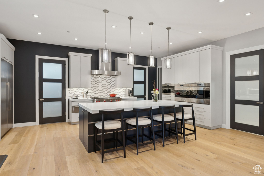 Kitchen with wall chimney exhaust hood, appliances with stainless steel finishes, tasteful backsplash, white cabinets, and recessed lighting