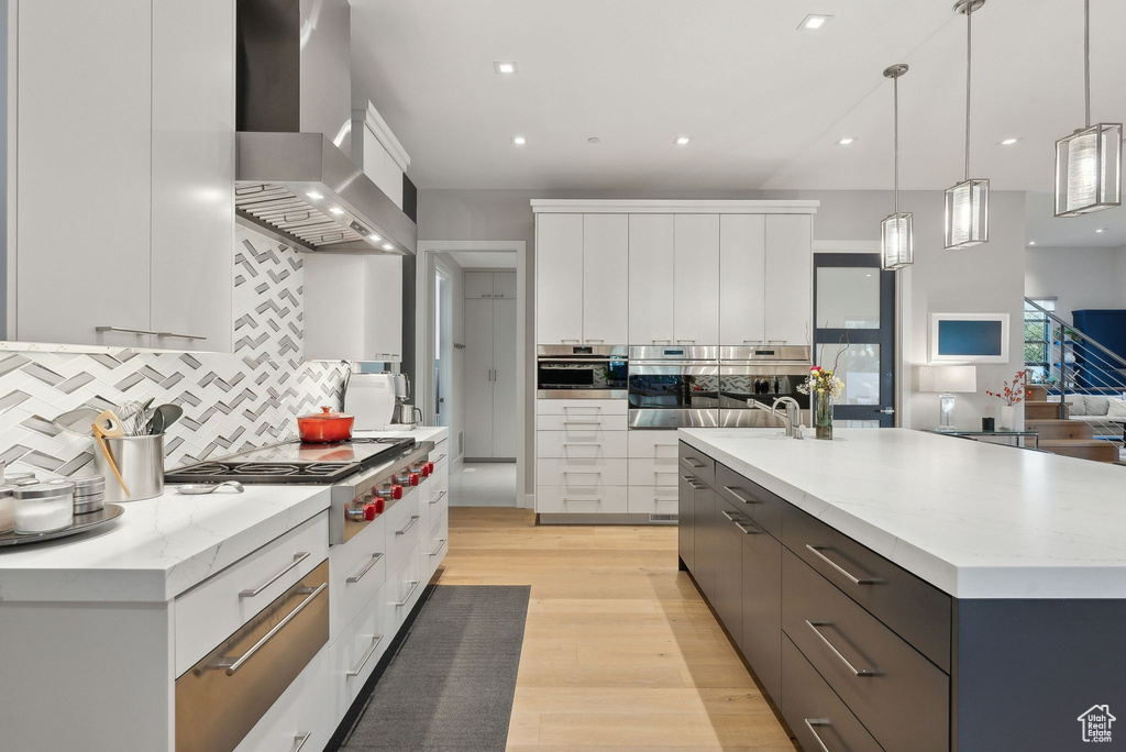 Kitchen featuring wall chimney exhaust hood, modern cabinets, white cabinetry, decorative backsplash, and light wood-type flooring