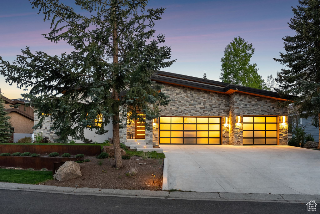 Modern home with stone siding, an attached garage, and driveway