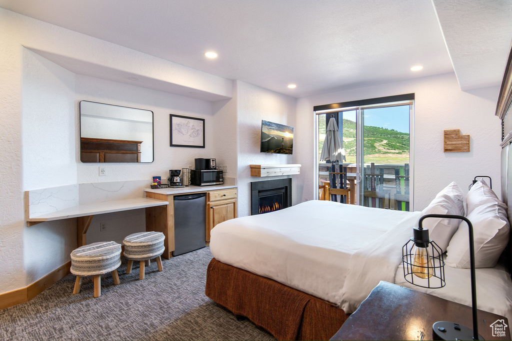 Carpeted bedroom featuring fridge, recessed lighting, a warm lit fireplace, and access to outside