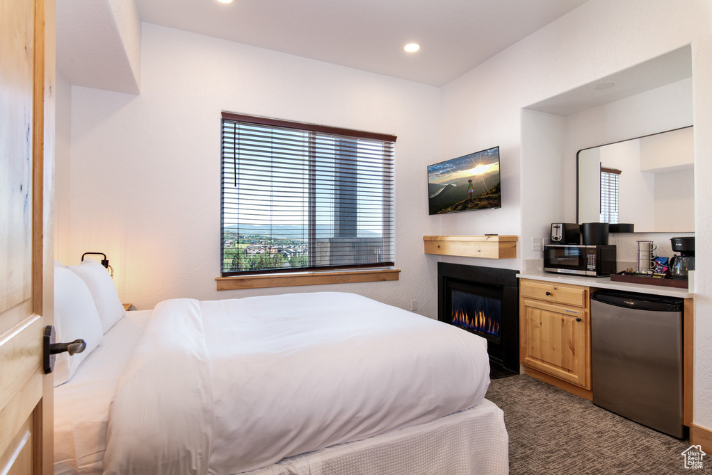 Bedroom with a glass covered fireplace, dark colored carpet, and recessed lighting