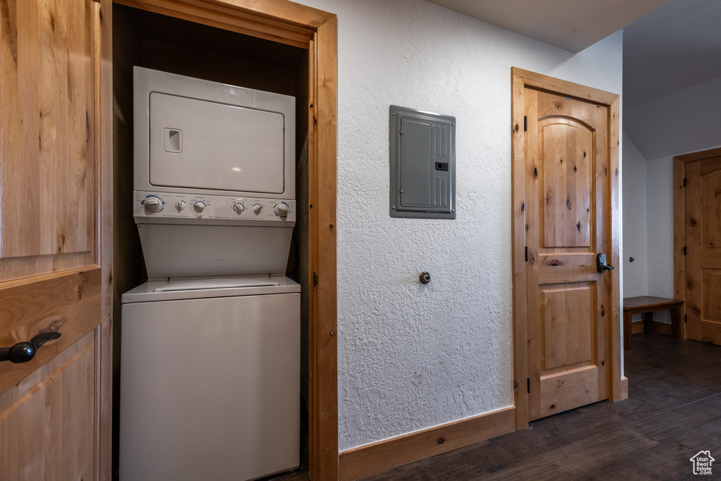 Laundry room featuring stacked washer / dryer, electric panel, dark wood-type flooring, and baseboards