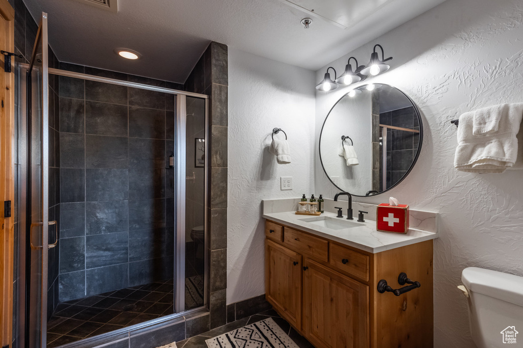 Full bath featuring toilet, a textured wall, vanity, a shower stall, and tile patterned floors