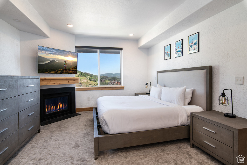 Bedroom with carpet, a glass covered fireplace, a textured wall, and recessed lighting