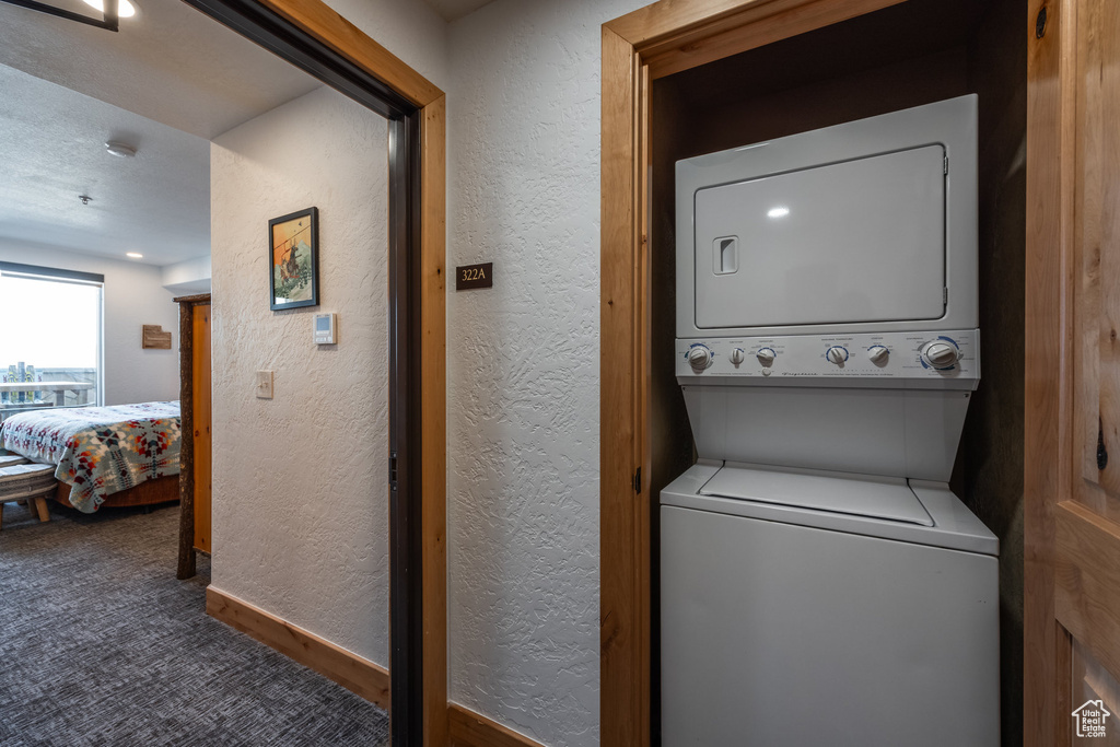 Laundry room featuring stacked washing machine and dryer, a textured wall, carpet, and baseboards