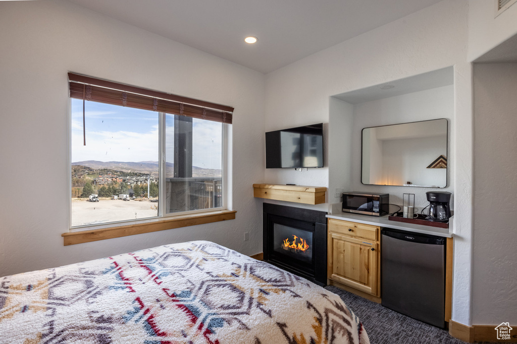 Bedroom with refrigerator, dark carpet, a glass covered fireplace, and recessed lighting