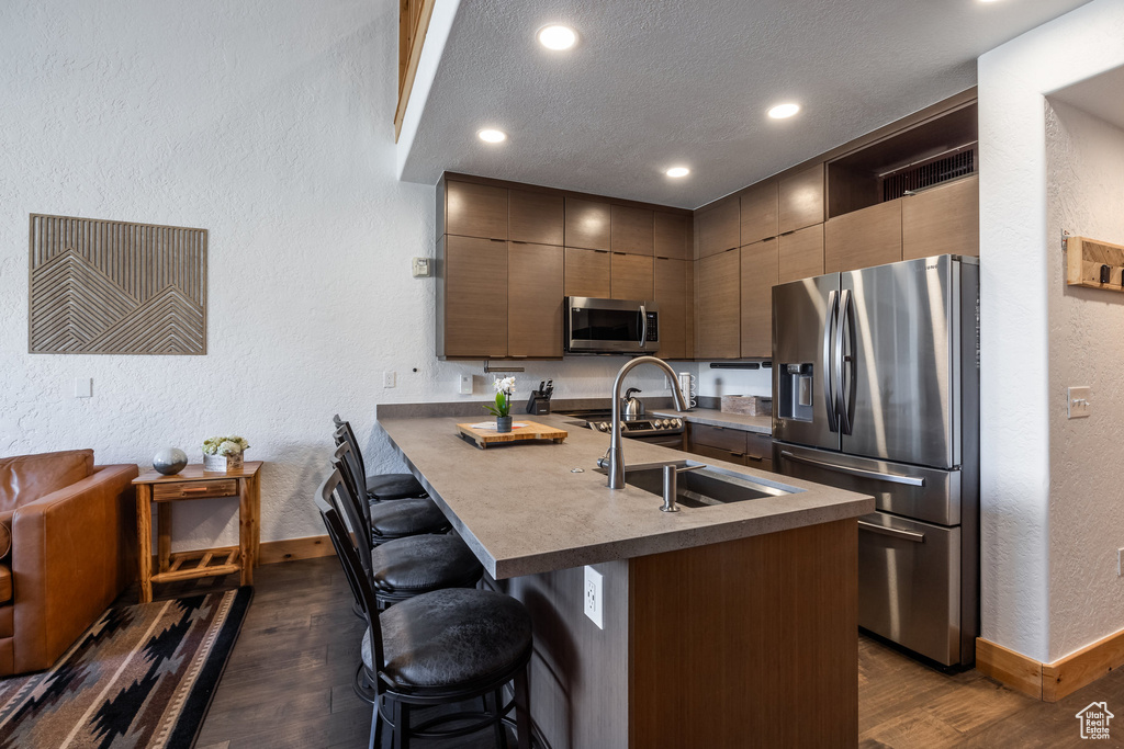 Kitchen featuring stainless steel appliances, baseboards, dark wood-style flooring, a sink, and a textured wall