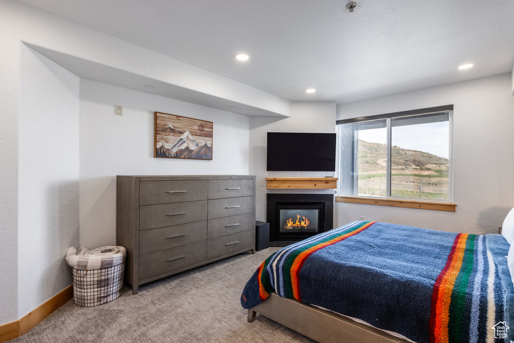 Carpeted bedroom featuring a glass covered fireplace and recessed lighting