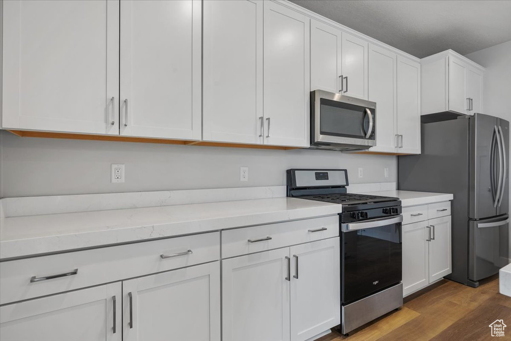 Kitchen featuring appliances with stainless steel finishes, dark wood-style flooring, and white cabinets