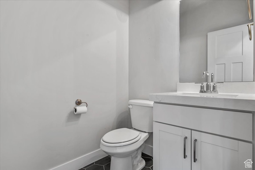 Half bathroom with baseboards, toilet, tile patterned flooring, and vanity