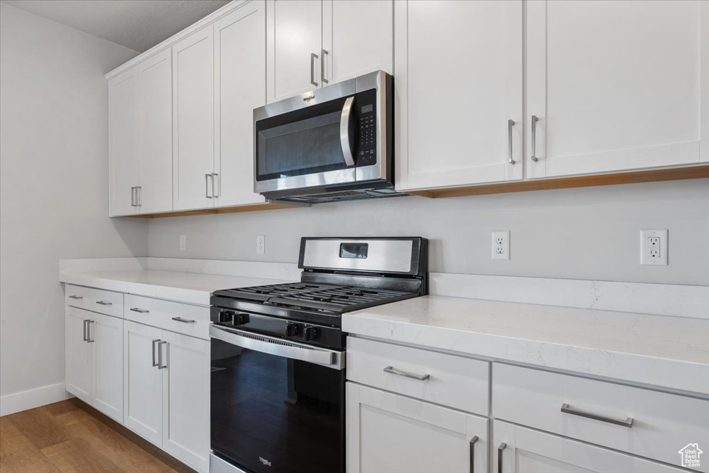 Kitchen featuring white cabinets, appliances with stainless steel finishes, wood finished floors, and baseboards