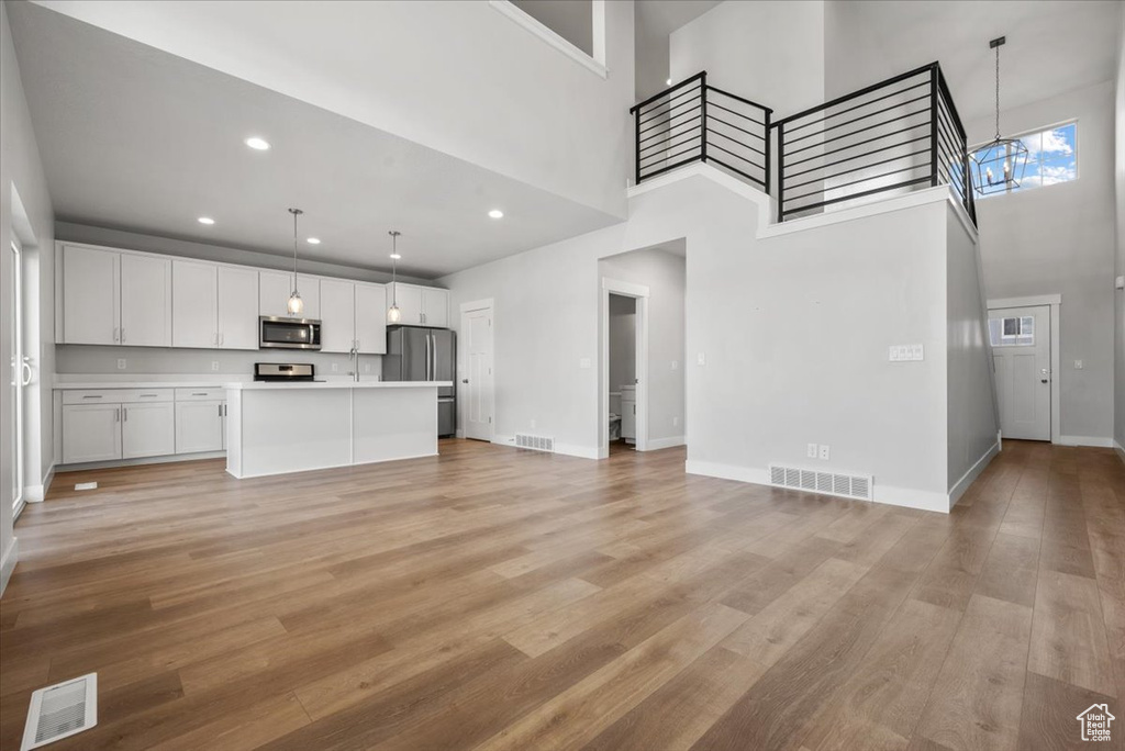 Unfurnished living room with visible vents, baseboards, light wood-style flooring, and a high ceiling