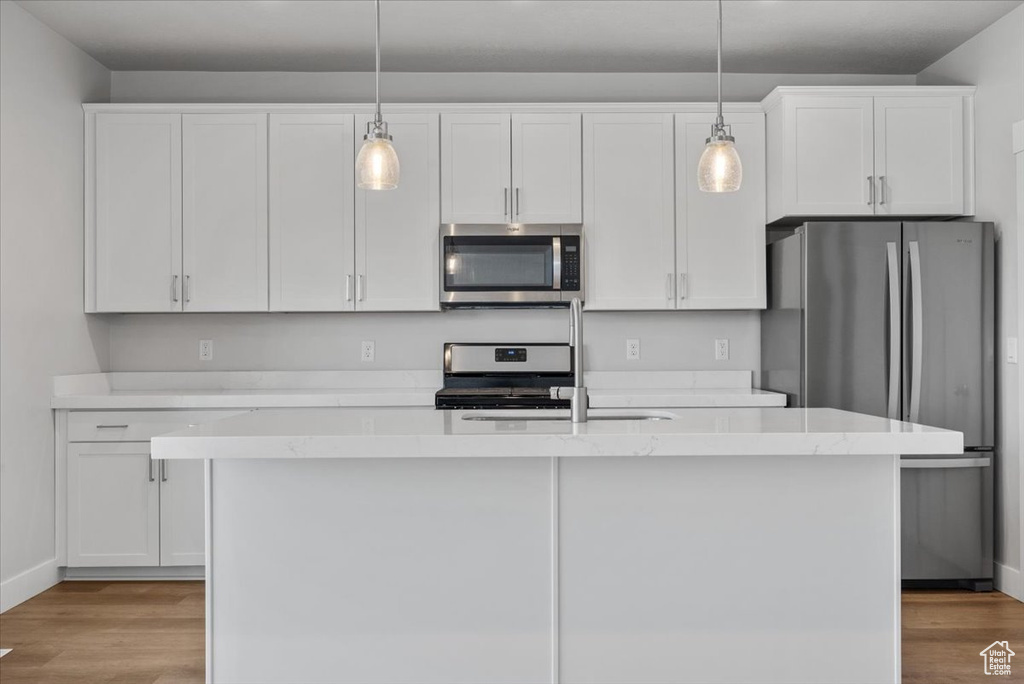 Kitchen with a sink, stainless steel appliances, light wood-type flooring, a center island with sink, and white cabinetry