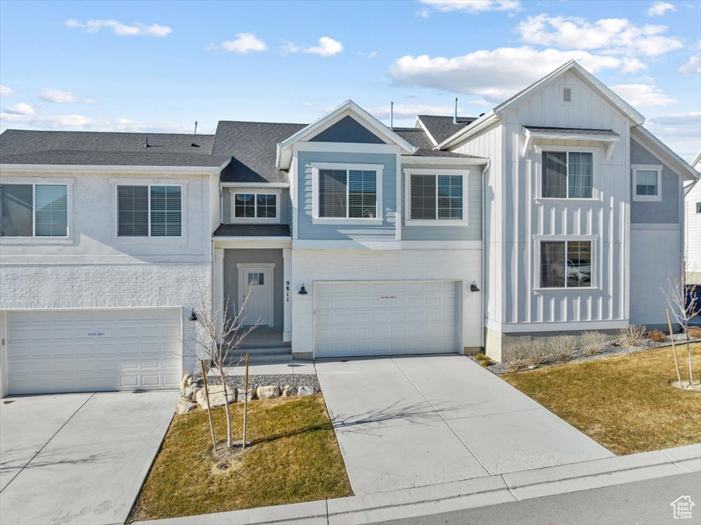View of front facade with a front yard, driveway, an attached garage, and board and batten siding