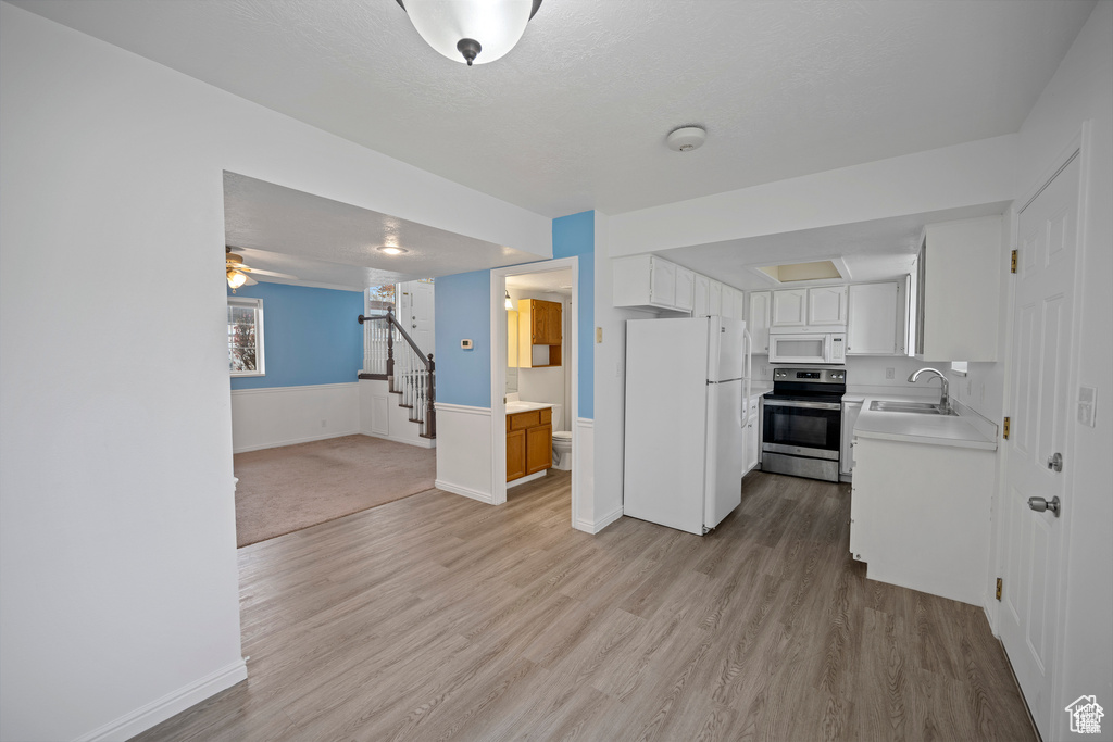 Kitchen with white appliances, light wood-type flooring, light countertops, open floor plan, and a wainscoted wall