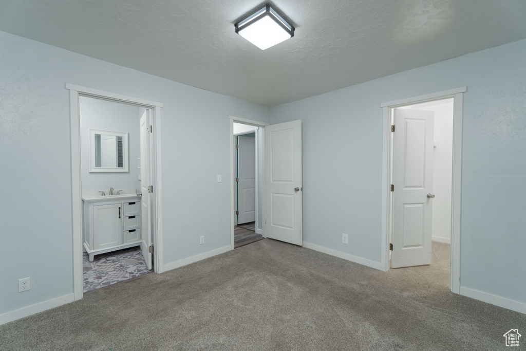 Unfurnished bedroom with a textured ceiling, sink, light carpet, and ensuite bath