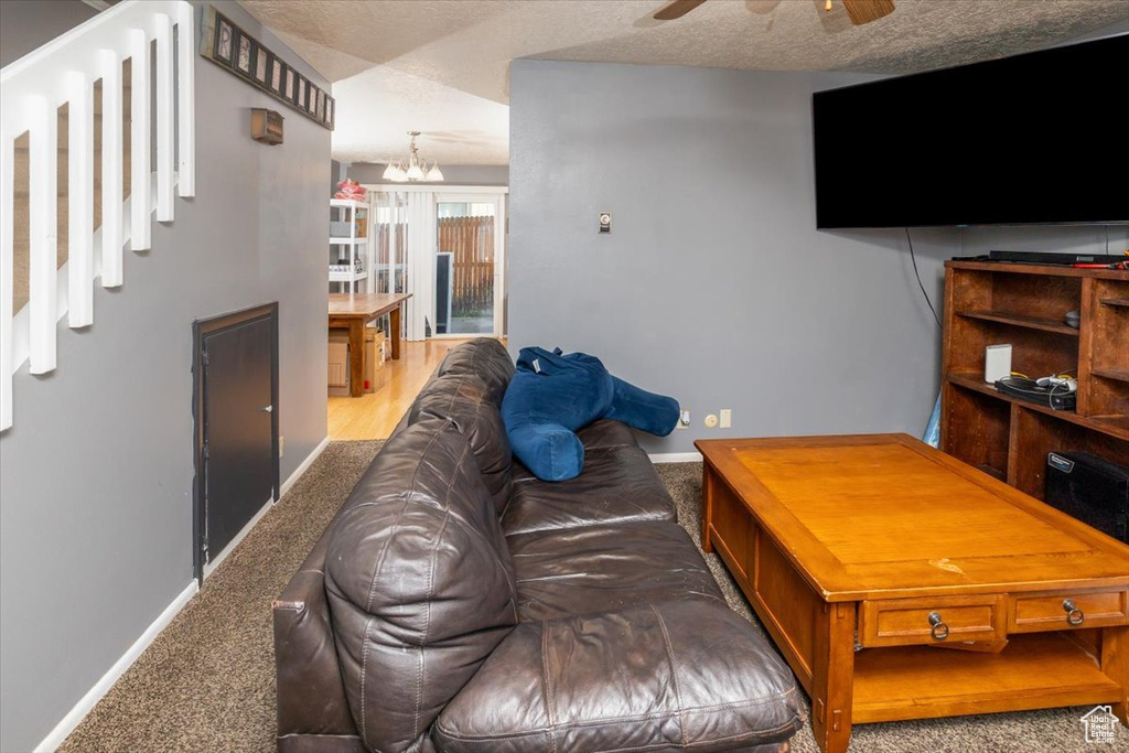 Living room featuring carpet, ceiling fan with notable chandelier, and a textured ceiling