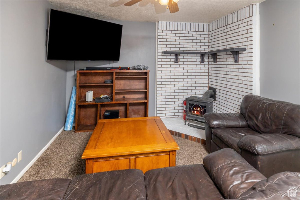 Carpeted living room featuring a textured ceiling, a wood stove, and ceiling fan