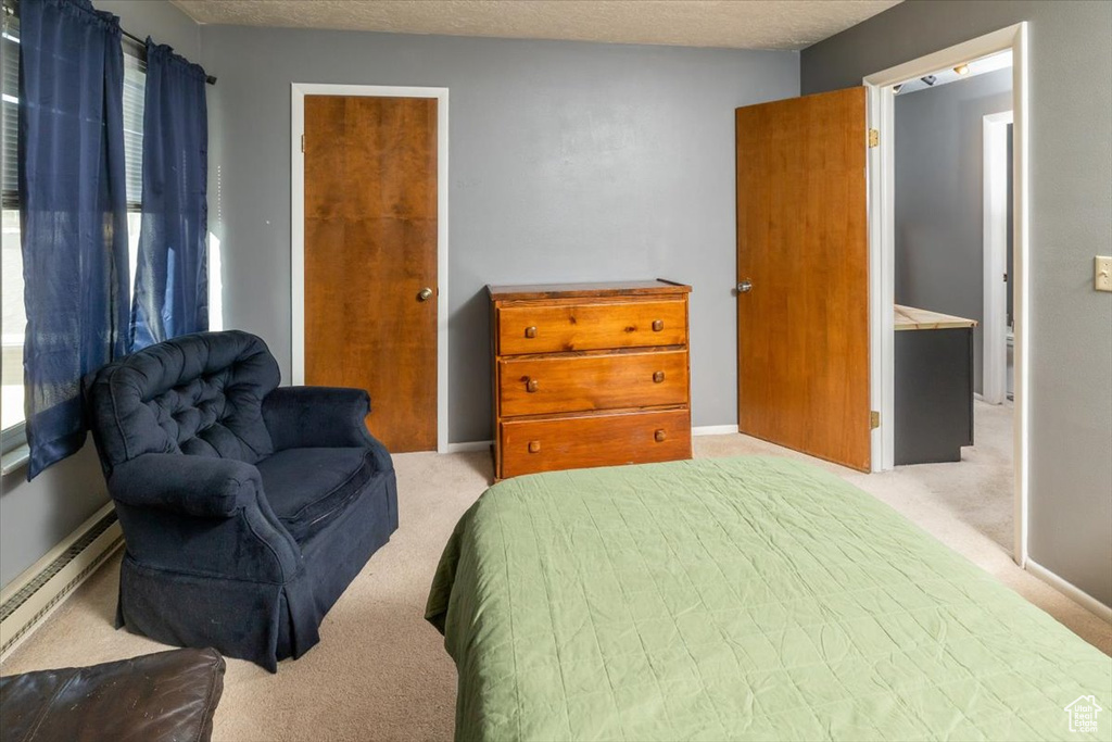 Bedroom with a textured ceiling, light colored carpet, a baseboard radiator, and ensuite bath