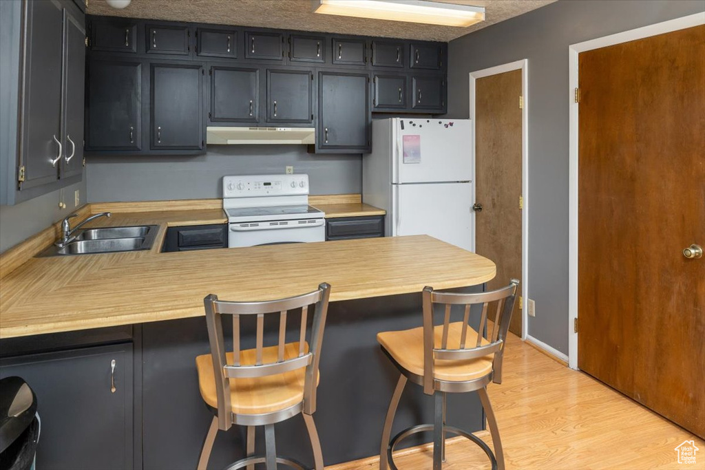 Kitchen with sink, kitchen peninsula, white appliances, a breakfast bar area, and light wood-type flooring