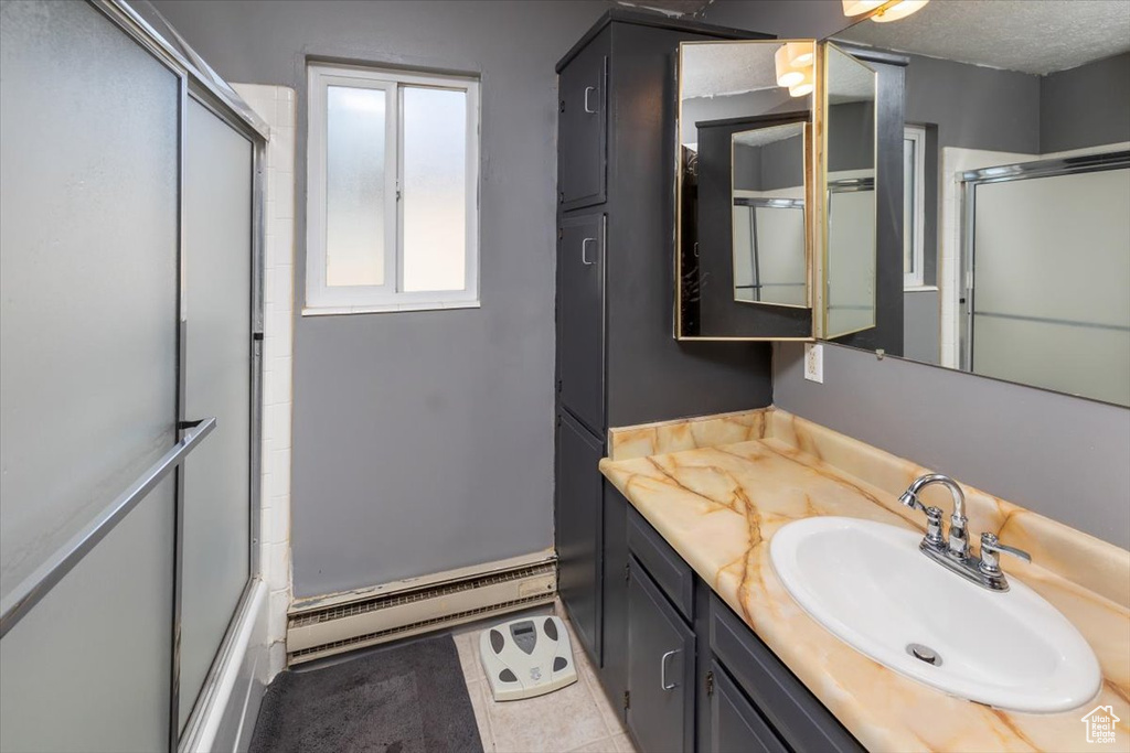 Bathroom with combined bath / shower with glass door, a textured ceiling, vanity, baseboard heating, and tile patterned flooring