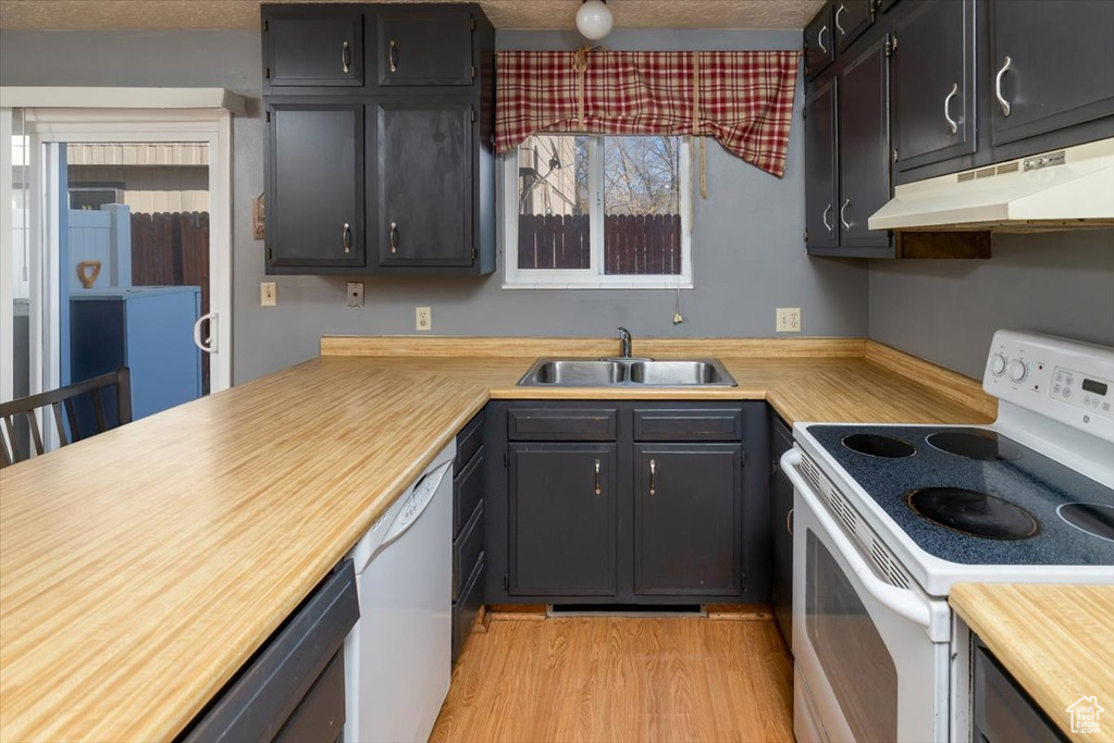 Kitchen with a textured ceiling, white appliances, light hardwood / wood-style floors, and sink