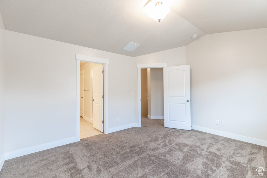 Unfurnished bedroom with ensuite bathroom, light carpet, and vaulted ceiling
