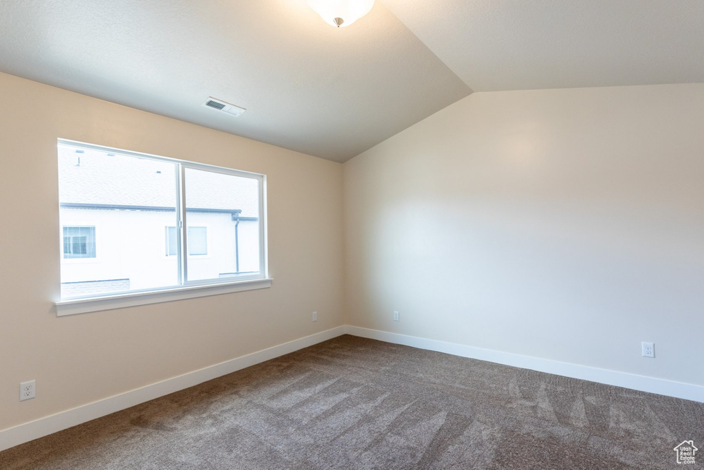 Spare room featuring carpet floors and vaulted ceiling