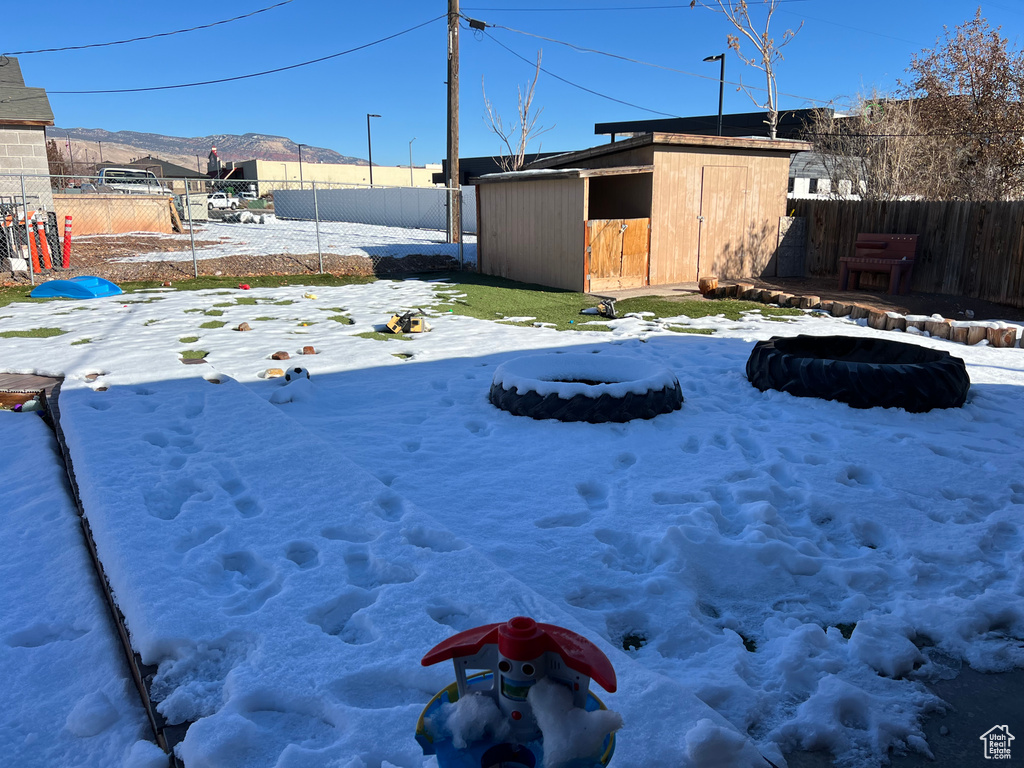 Yard layered in snow featuring a mountain view and a storage unit