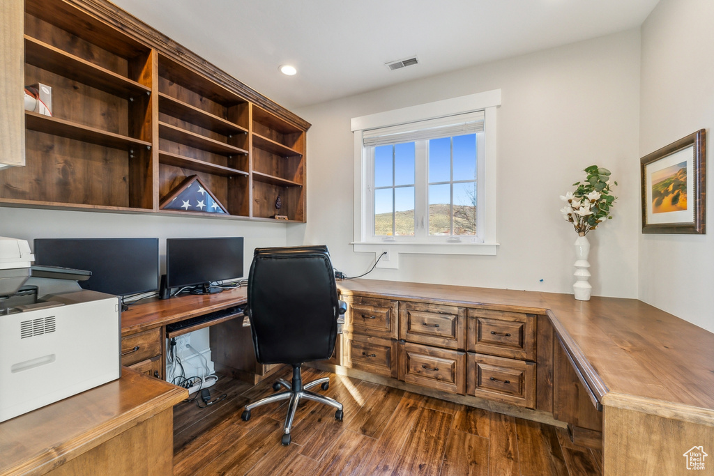 Home office with built in desk and dark wood-type flooring