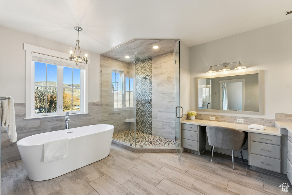 Bathroom featuring separate shower and tub, vanity, tile walls, and a notable chandelier