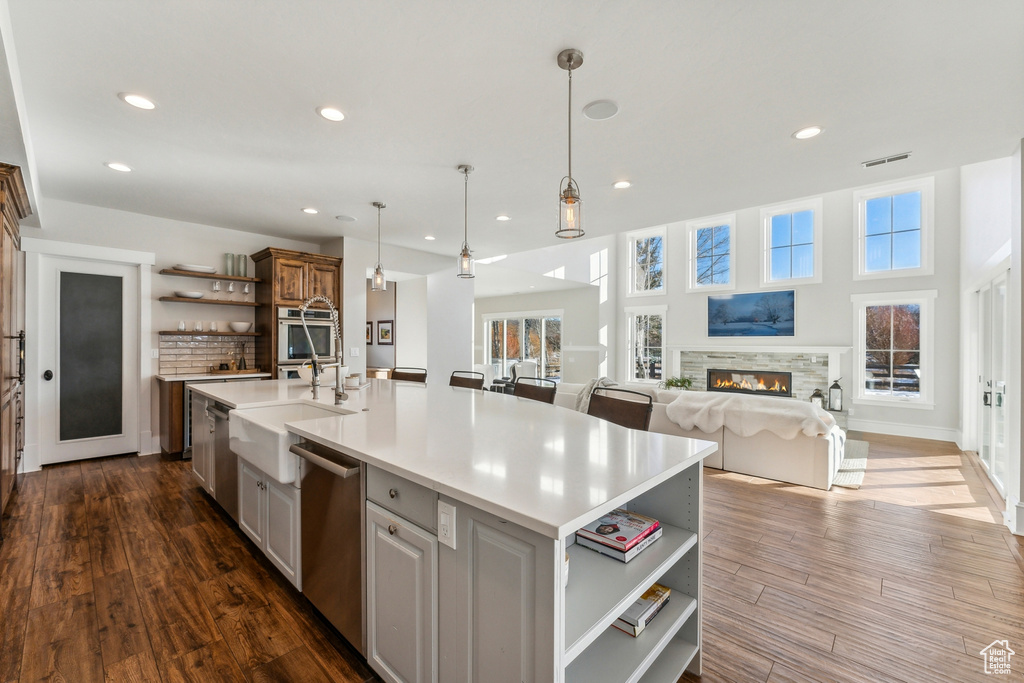 Kitchen featuring hanging light fixtures, dark wood-type flooring, stainless steel appliances, a fireplace, and a center island with sink