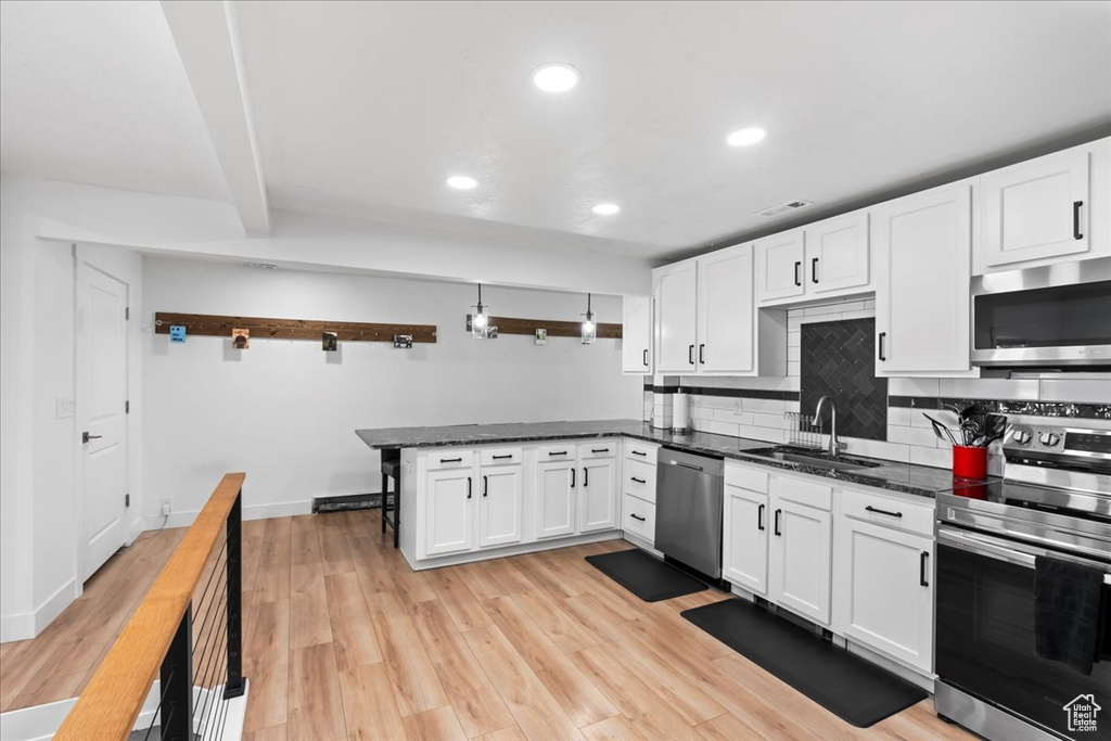 Kitchen featuring kitchen peninsula, white cabinetry, light hardwood / wood-style flooring, and appliances with stainless steel finishes