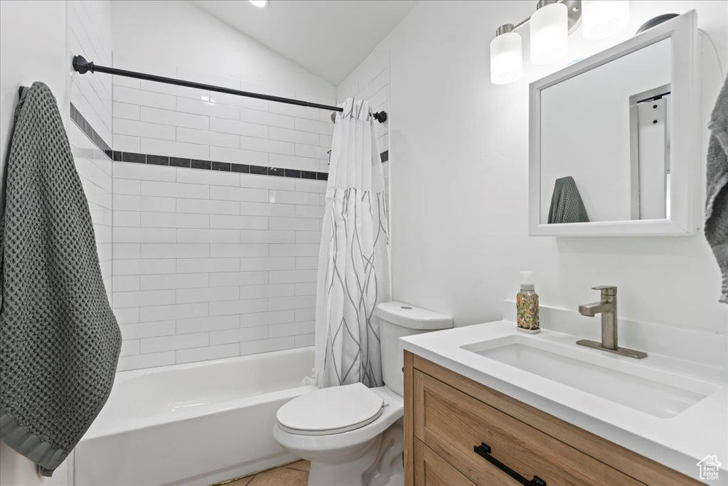 Full bathroom with tile patterned floors, vanity, vaulted ceiling, shower / bathtub combination with curtain, and toilet