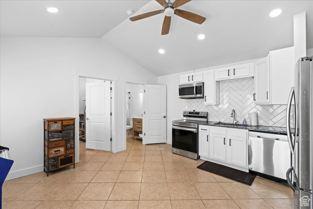 Kitchen featuring stainless steel appliances, ceiling fan, sink, white cabinetry, and lofted ceiling